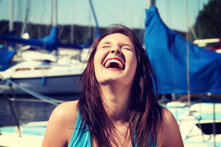 Happy girl in front of yacht boat is laughing with closed eyes.