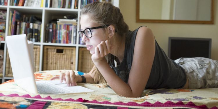 Teenage girl lying on front using laptop