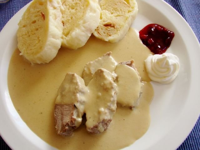 Svíčková na smetaně served with dumplings, whipped cream and cranberries