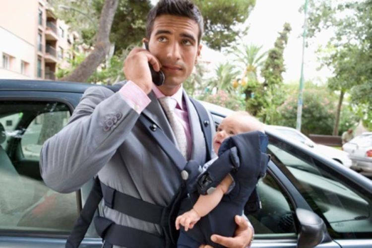 Businessman talking on cell phone and holding baby in baby carrier