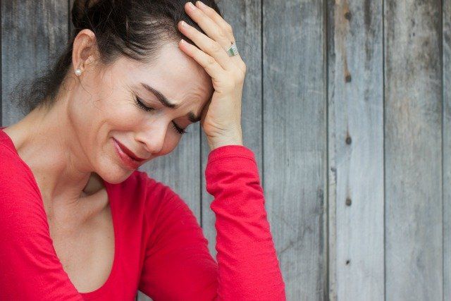 A very upset and lonely woman sitting down crying against a wall