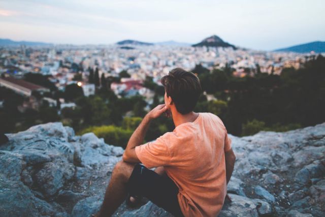 man-in-orange-shirt-sitting-on-gray-rocks