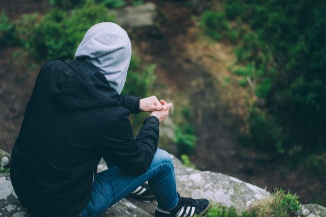 person-wearing-black-hoodie-sitting-on-gray-rock