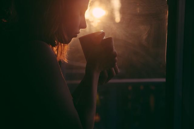 woman-holding-cup-near-window-reflected-with-sun