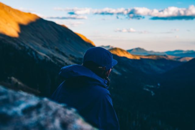 man-in-blue-hoodie-standing-on-mountain-cliff-during-daytime