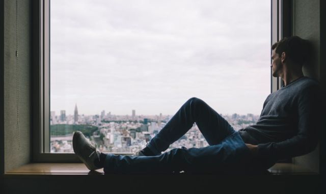 man-sitting-near-window-viewing-outside-buildings-during-daytime