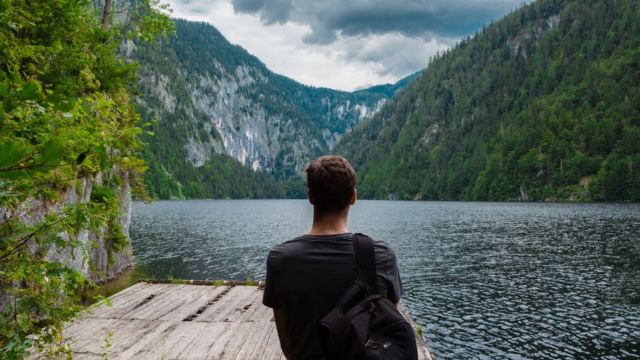 man-carrying-black-backpack-standing-on-brown-wooden-dock-during-daytime