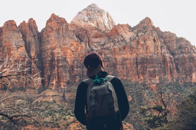 man-wearing-gray-backpack-standing-in-front-of-rocky-mountain-during-daytime