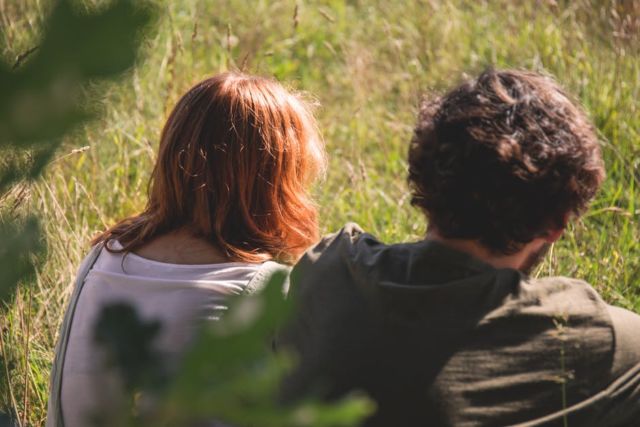 people-photography-of-man-and-woman-sitting-on-green-grass-field