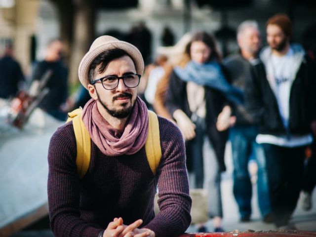 man-sitting-next-to-couple-of-person-walking-on-the-street-during-daytime