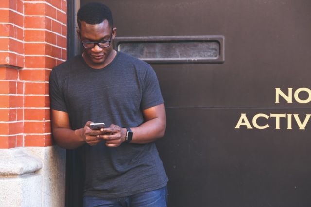 man-in-grey-crew-neck-t-shirt-leaning-on-brown-brick-wall-holding