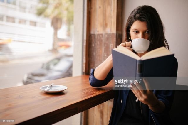 Girl Drinking Coffee and Reading Book in Cafe