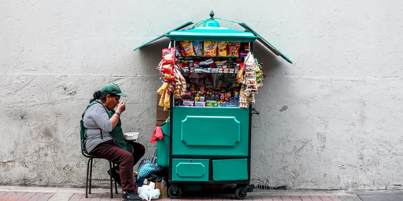 Women Eating While Seated Next to Mobile Shop Cart