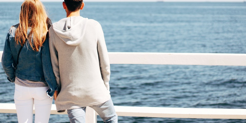 Man and woman beside hand rail beside body of water