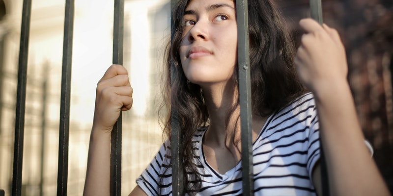 Sad isolated young women looking away through fence 